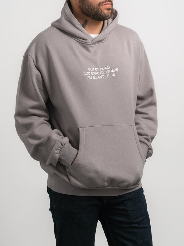 Model wearing SecondHand Kids Out of Place Hoodie — relaxed fit, drop shoulder, mid-weight fleece, box hoodie style. Embroidered text reads ‘Out of place, and exactly where I’m meant to be’