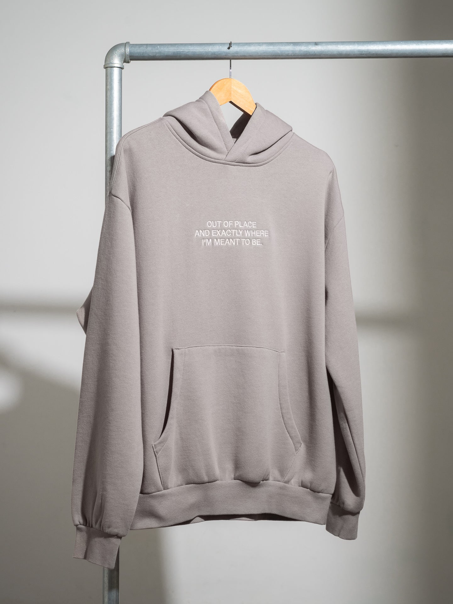Gray SecondHand Kids "Out of Place" hoodie with text on a hanger against a neutral background
