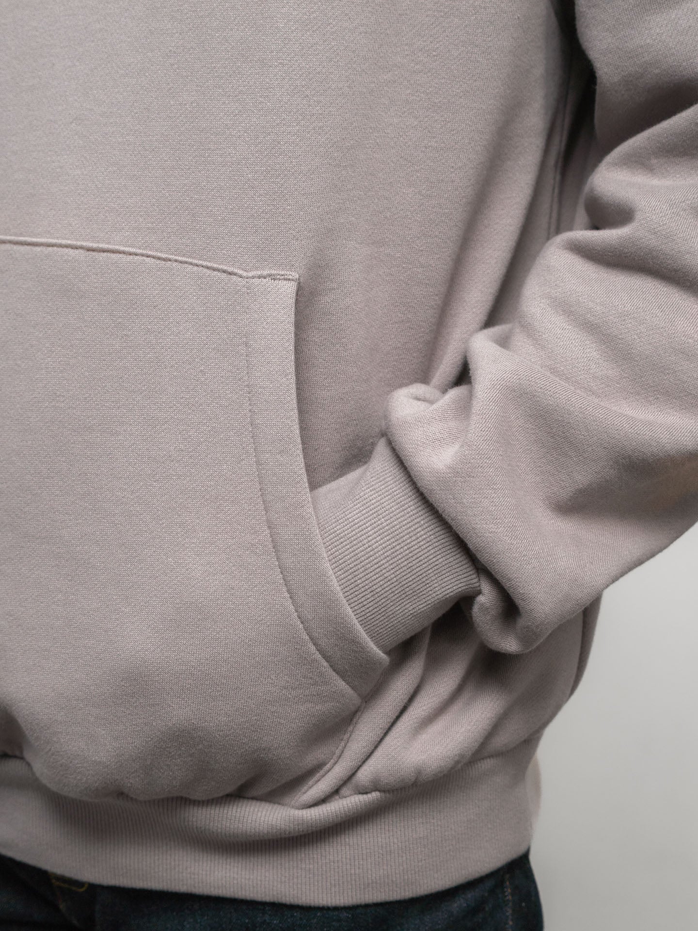 Close-up of a light gray SecondHand Kids 'Out of Place' hoodie with a pocket on a plain background