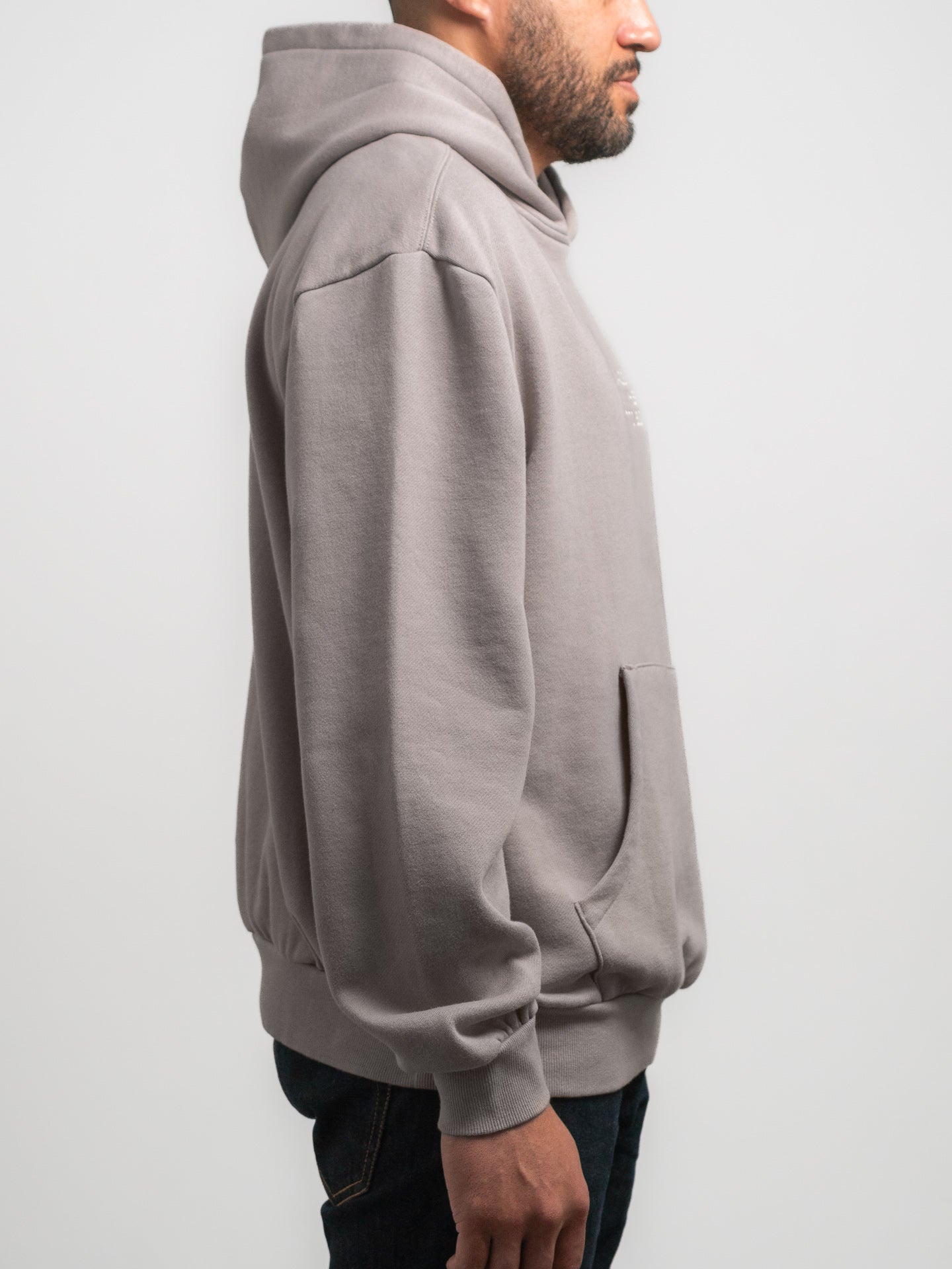 Person wearing a grey SecondHand Kids hoodie on a light gray background facing the side.